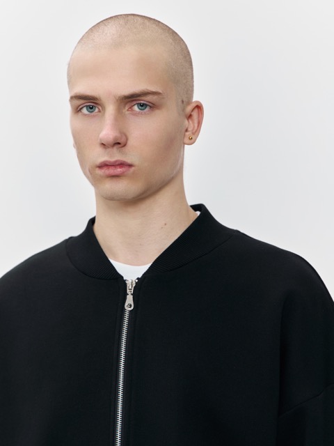 Мужчина в минималистичном чёрном бомбере из плотного трикотажа, показывающий качество молнии и аккуратный крой. Универсальная модель для корпоративного мерча и брендированных коллекций.