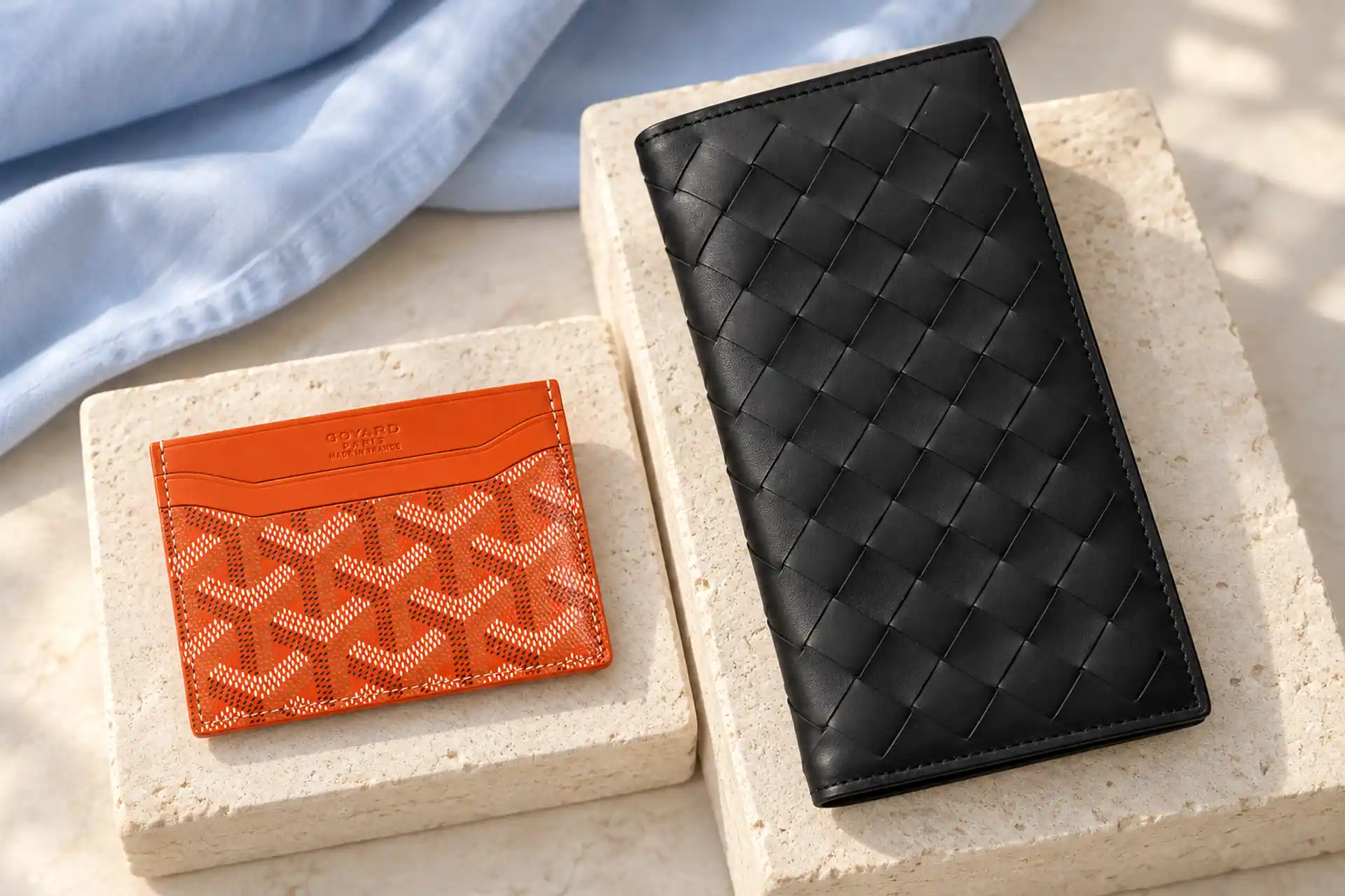 Оранжевый картхолдер Goyard и чёрный плетёный купюрник Bottega Veneta на светлых подставках