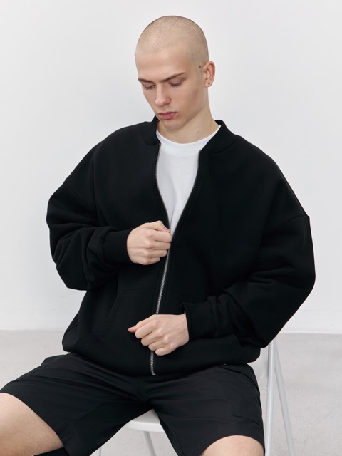 Мужчина в чёрном трикотажном бомбере на молнии, демонстрирующий посадку и детали изделия. Стильная модель корпоративной одежды для мерча и брендирования.