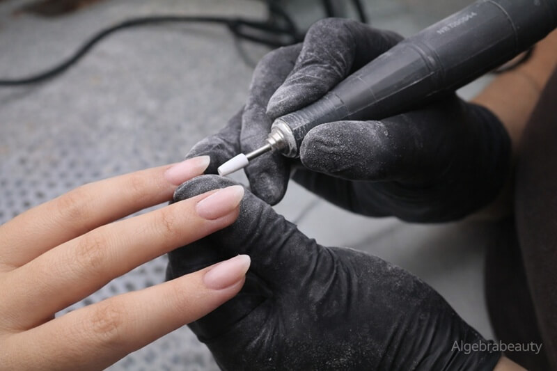 Мастер выполняет коррекцию гель-лака фрезой &mdash; обработка ногтя в салоне