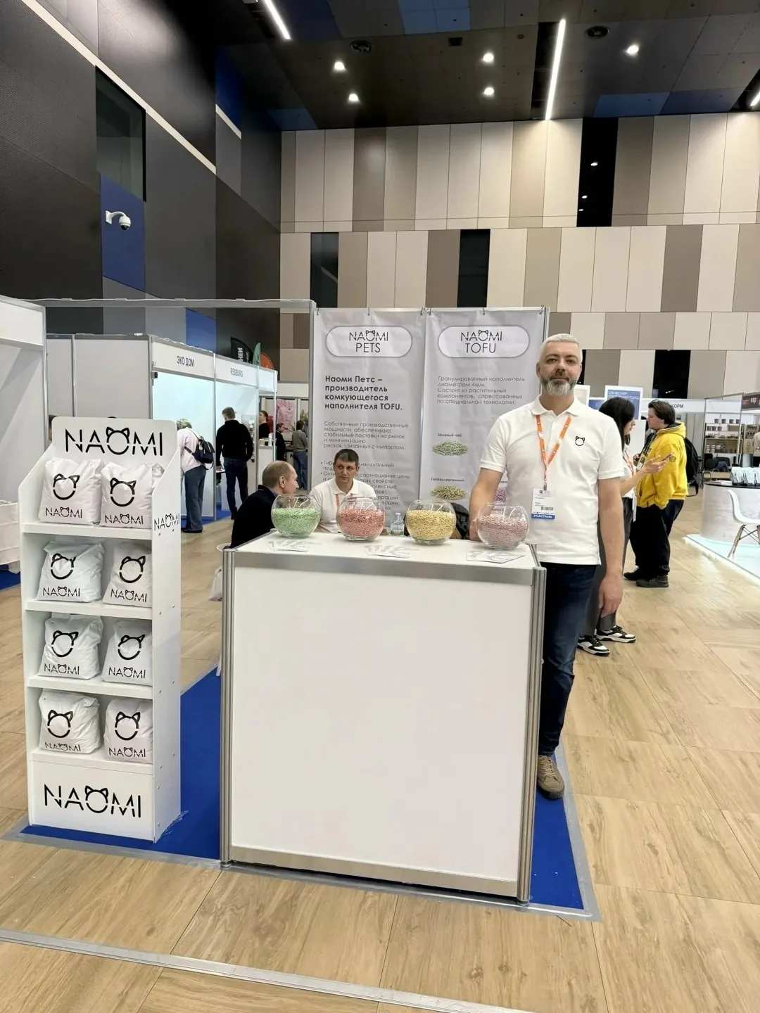 Стенд NAOMI с продукцией и сотрудник в белой футболке