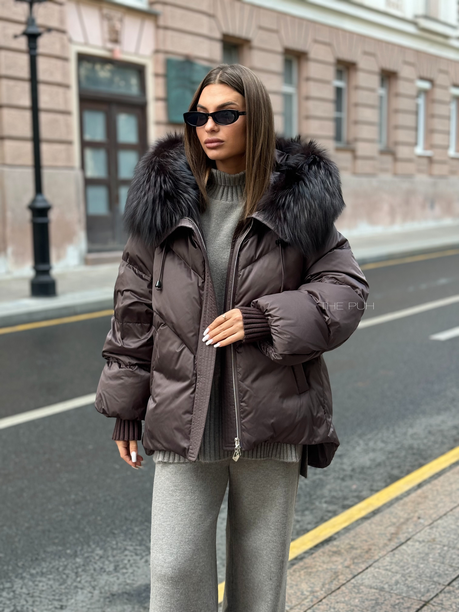 Шоколадный пуховик с удлиненной спинкой и мехом енота