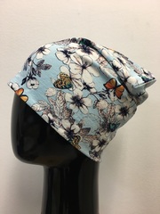 Удлиненная шапочка бини из вискозного трикотажа с белыми цветами, листиками и разноцветными бабочками на светло-голубом фоне.