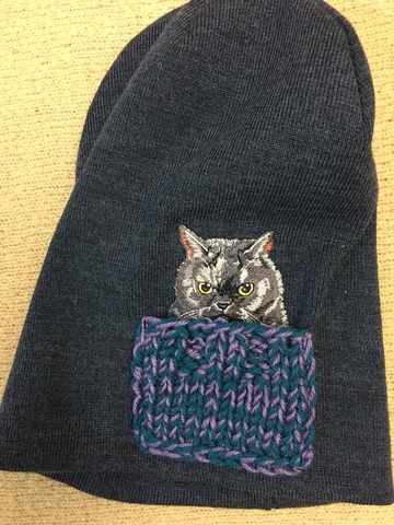 Зимняя двойная удлиненная (высота около 28 см) шапочка, сбоку декорирована нашивкой в виде котика, который уютно устроился в связанном вручную кармашке. Цвет шапочки - джинсовый меланж.