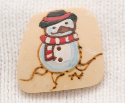Пуговица-открытка с нарисованным снеговиком в чёрной шляпе на песочном фоне