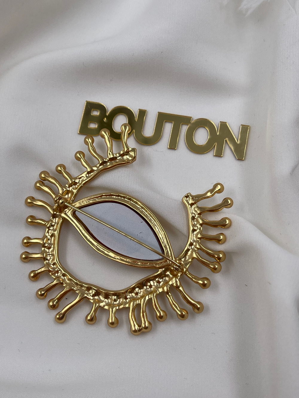 Брошь Скиап. золотистая в форме глаза с подковой из ресниц со стразами красный