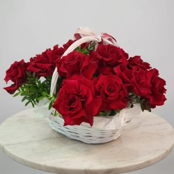 15 бордовых роз в плетеной корзине с добавлением зелени.