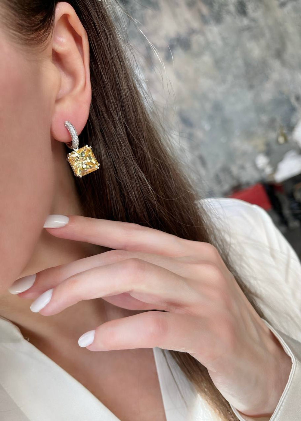 Спокойный и благородный цвет кристалла побуждает купить серьги с микро фианитами белого цвета и желтым центральным камнем в виде квадрата. С ними можно создать десятки вечерних и повседневных образов. Чтобы акцентировать внимание на квадратных серьгах из серебра 925-й пробы с желтым фианитом, можно дополнить их кольцом или кулоном с большим камнем в том же стиле или оттенке. Особенно советуем приобрести изделия девушкам с карими глазами. Благодаря скромным на первый взгляд серебряным украшениям цвет глаз станет еще выразительней.  Заказать серьги из серебра с желтыми фианитами вы можете в нашем интернет-магазине по демократичной цене. Доставка ювелирного изделия возможна как по столице, так и в любую точку страны.