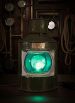 Навигационный огонь WOODandROOT 1957 года с мягким сине-зелёным свечением, размещённый в тёмном корабельном интерьере.