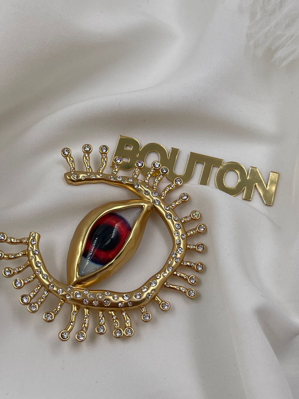 Брошь Скиап. золотистая в форме глаза с подковой из ресниц со стразами красный