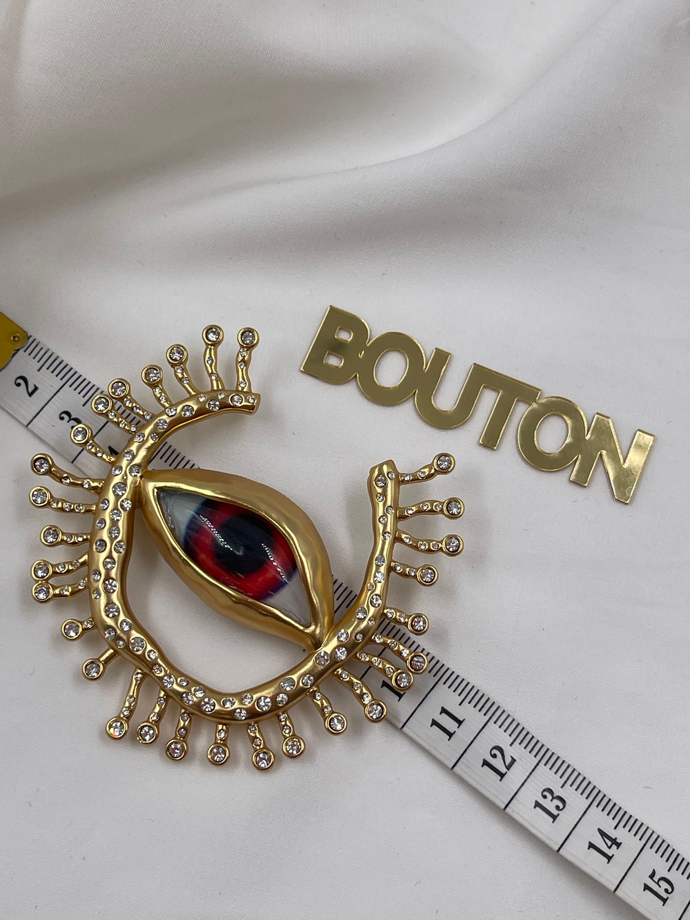 Брошь Скиап. золотистая в форме глаза с подковой из ресниц со стразами красный