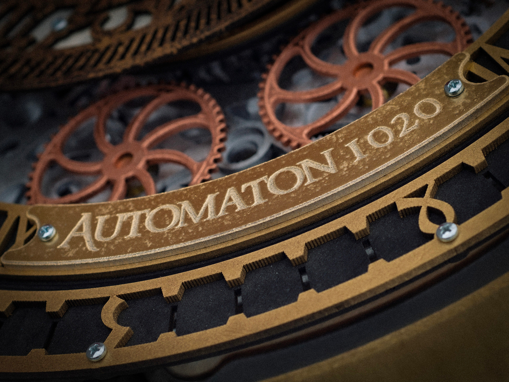Деталь настенных часов WOODandROOT Automaton Prague, выгравированная надпись Automaton 1020 и шестерёнки под стеклом