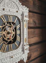 Фрагмент часов WOODandROOT «Автоматон Вологда» на деревянной стене, с детальной резьбой и золотистым декоративным механизмом на циферблате.