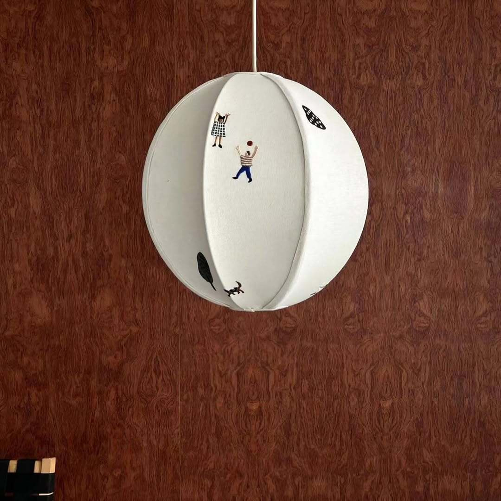 Нежный подвесной светильник в виде круглого абажура с минималистичными рисунками людей и деревьев.