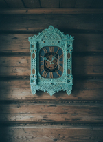 Мятные резные часы-наличник WOODandROOT на старой деревянной стене, мягкая тень подчёркивает глубину резьбы и характер слоистой окраски.