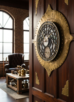 Часы WOODandROOT «Башня Волшебника» с двойным циферблатом размещены на резной двери; на фоне виден уютный интерьер с креслом и столиком.