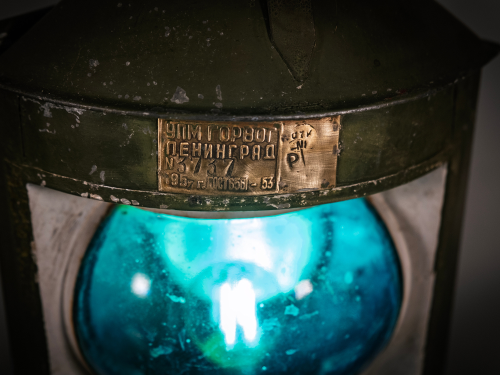 Навигационное сине-зелёное стекло и латунная табличка судового фонаря WOODandROOT 1957 года с выраженными следами времени.