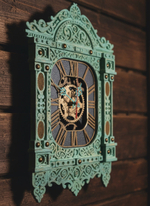 Мятные часы-наличник WOODandROOT с резным орнаментом, снятые в боковом ракурсе на фоне деревянной стены в тёплом рассеянном свете.