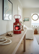 Интерьерный морской светильник WOODandROOT из корабельного фонаря 1957 года на деревянной консоли в светлой комнате с канатами и картами.