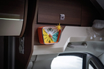 Настенные мини‑часы Camper Starburst 15×12 см с оранжевым корпусом и звездой‑компасом, прикреплены к деревянной панели автодома, создают уют и яркий ретро стиль.