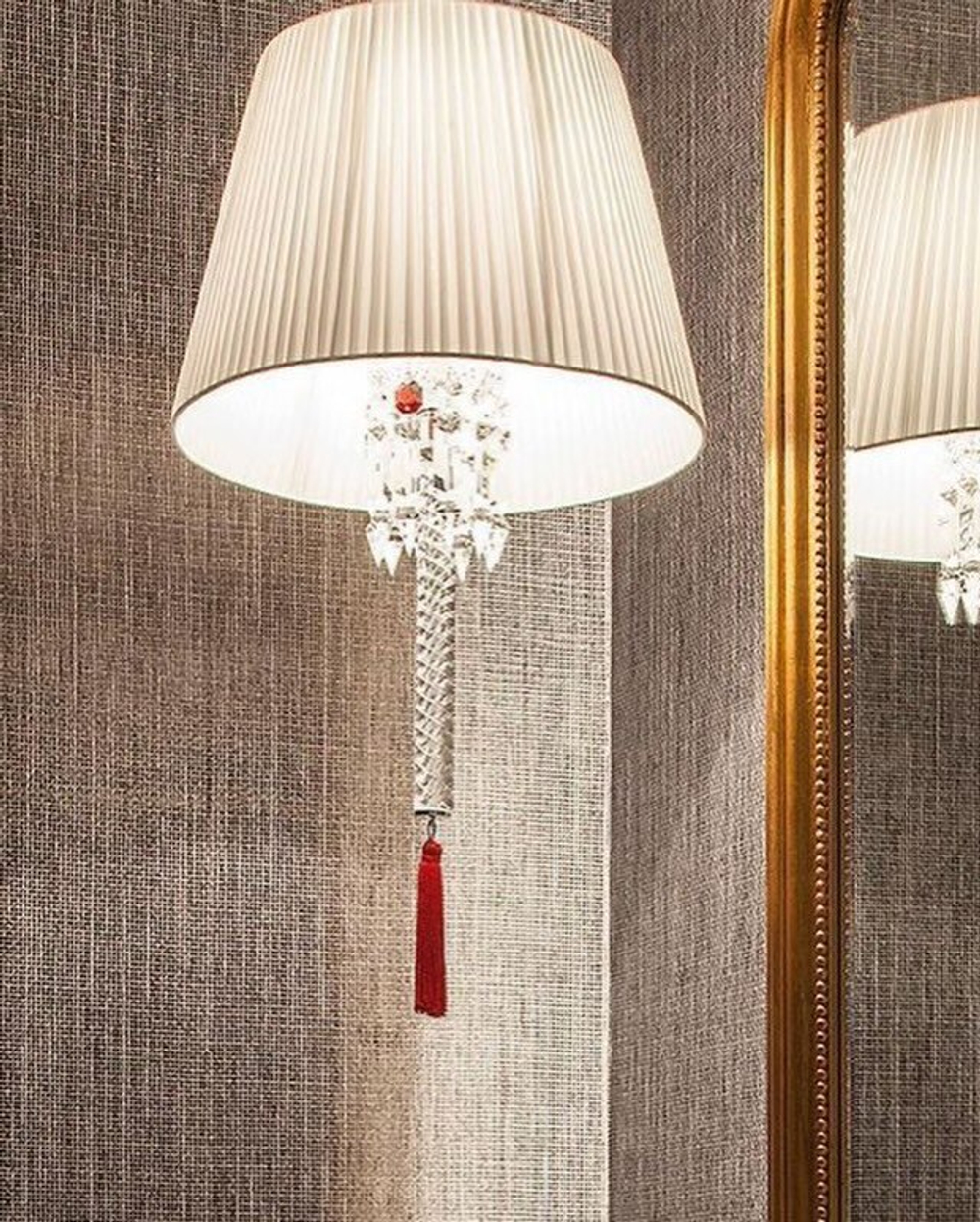 Изысканное люстра Baccarat с белым плиссированным абажуром, хрустальной ножкой и акцентной красной кистью.