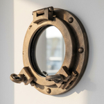 WOODandROOT зеркало-иллюминатор ручной работы с латунным декором в тёплом естественном свете на белой стене, морской интерьер.