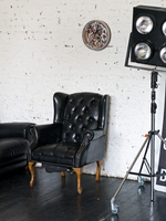 Настенные часы WOODandROOT Automaton 1277 Tourbillon на белой кирпичной стене рядом с кожаным креслом и студийным осветительным оборудованием.