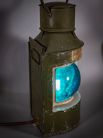 Корабельный фонарь WOODandROOT 1957 года с мягким сине-зелёным свечением, показывающий форму корпуса и характерную патину металла.
