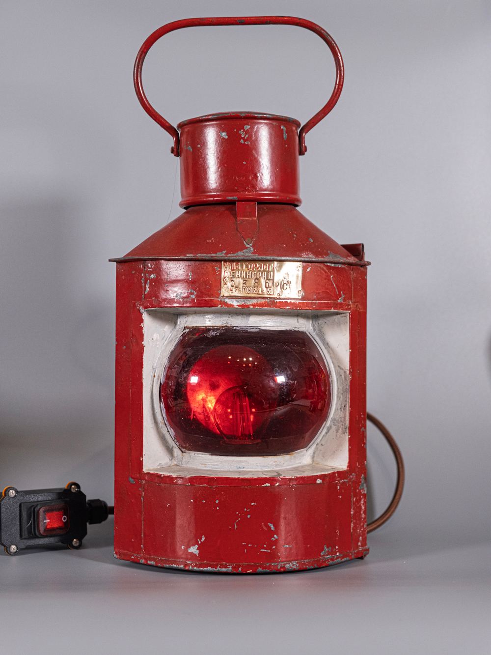 Судовой навигационный фонарь WOODandROOT 1957 года в красном металлическом корпусе и оригинальным стеклом, снятый на светлом нейтральном фоне.